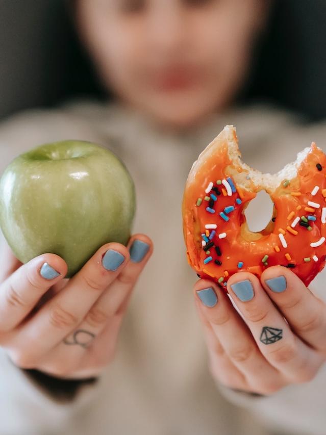 woman holding a green apple and a pink donut side by side